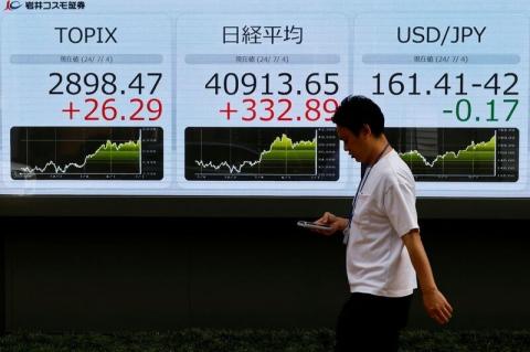 FILE PHOTO: A man walks past a monitor displaying the Topix share average, Nikkei share average and the Japanese yen exchange rate against the U.S. dollar, outside a brokerage in Tokyo, Japan, July 4, 2024. REUTERS/Kim Kyung-Hoon/File Photo